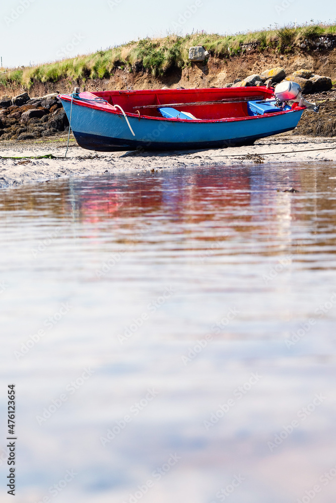 Naklejka premium Small blue color fishing boat with red painted interior on a sandy beach at low tide. Food supply chain industry.
