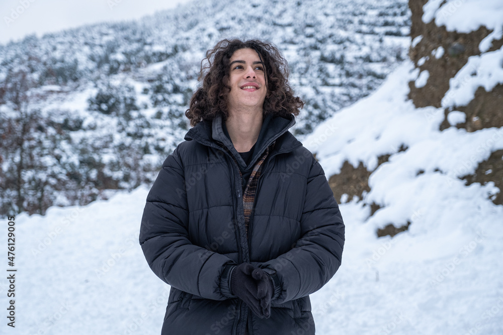 handsome and long haired smiling man in black coat standing in snowy weather in front of natural background handsome and long haired smiling man in black coat standing in snowy weather in front of natural background