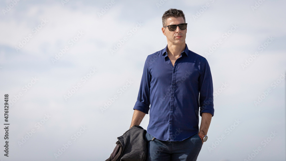 Portrait of a young classy entrepreneur relaxing alone along the Lisbon riverside in Portugal. Classy business man wearing a blue elegant shirt and formal outfit. Successful lifestyle concept. Portrait of a young classy entrepreneur relaxing alone along the Lisbon riverside in Portugal. Classy business man wearing a blue elegant shirt and formal outfit. Successful lifestyle concept.