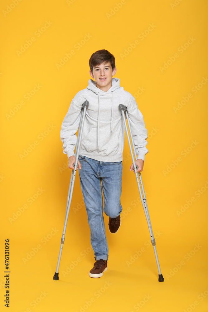 Teenage boy with injured leg using crutches on yellow background Teenage boy with injured leg using crutches on yellow background