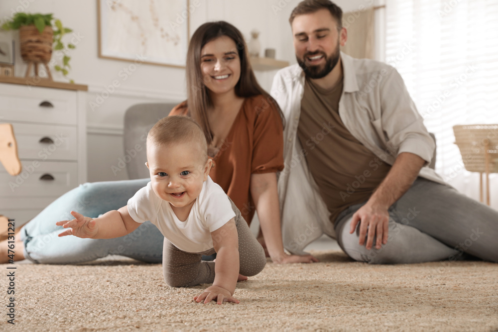 Happy parents watching their baby crawl on floor at home Happy parents watching their baby crawl on floor at home