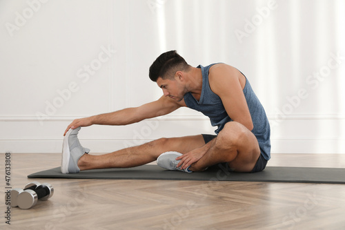 Handsome man stretching on yoga mat indoors