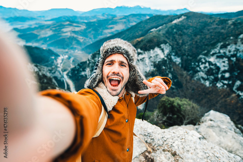 Hiker with backpack taking selfie on the top of the mountain - Happy man takes portrait picture outdoors enjoying winter sunny day - Sport, technology and lifestyle concept