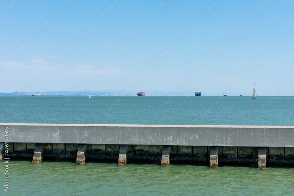 Concrete harbor wave barrier in San Francisco Bay. Blurred container ships fully loaded are anchored on horizon