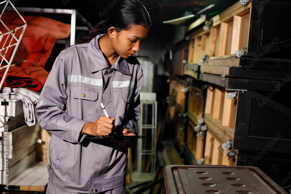 Asian 20s woman in grey uniform check count items in warehouse storage room. Maintenance Service