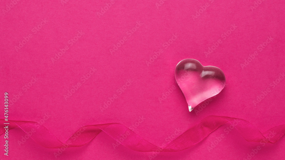 A figure of a glass heart and a ribbon on a pink background. The concept of Valentine's Day. A figure of a glass heart and a ribbon on a pink background. The concept of Valentine's Day.