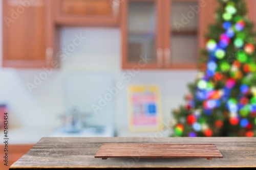 Wooden tabletop with cutting board and blurred kitchen with Christmas tree. Background for display or montage your products.