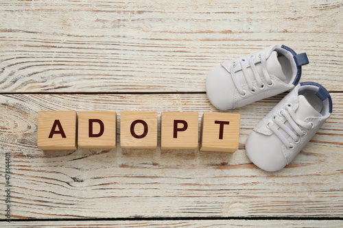 Word Adopt made of cubes and child shoes on white wooden table, flat lay photo