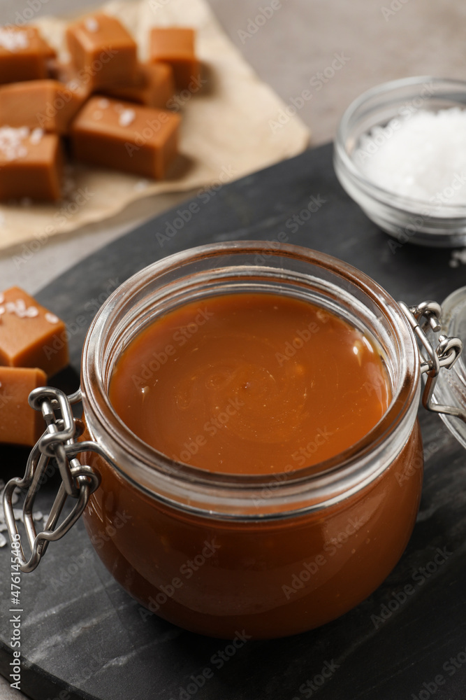 Tasty salted caramel in glass jar on grey table, closeup Tasty salted caramel in glass jar on grey table, closeup