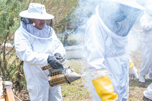 A woman beekeeper puts smoke with the smoker to a companion to scare away the bees