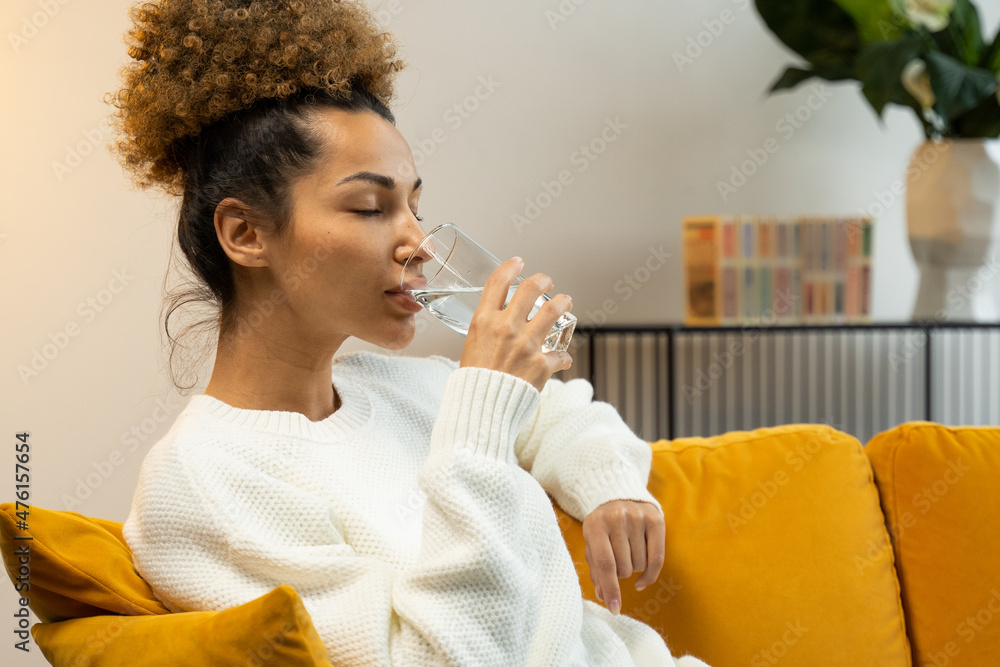 Ταπετσαρία Young black woman drinking a glass of water sitting on the sofa in the living ro