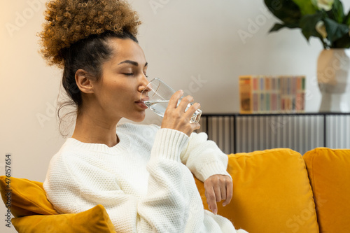 Young black woman drinking a glass of water sitting on the sofa in the living room