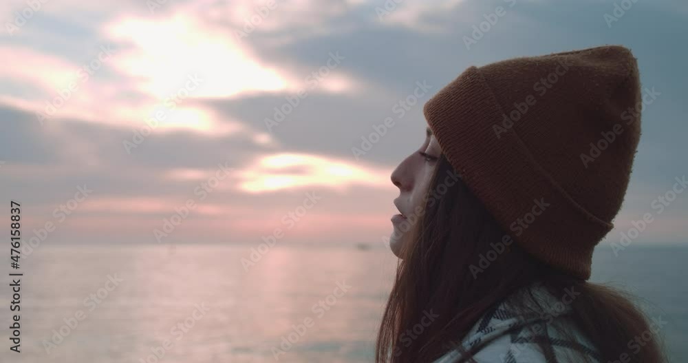 The profile of a female wearing a bonnet and looking at the sea at sunset. She sighs and turns her head slightly. The profile of a female wearing a bonnet and looking at the sea at sunset. She sighs and turns her head slightly.