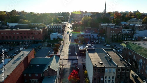 Rising aerial establishing shot of town in USA during golden hour light. Business office buildings and church steeple dot skyline during colorful autumn fall foliage season. photo