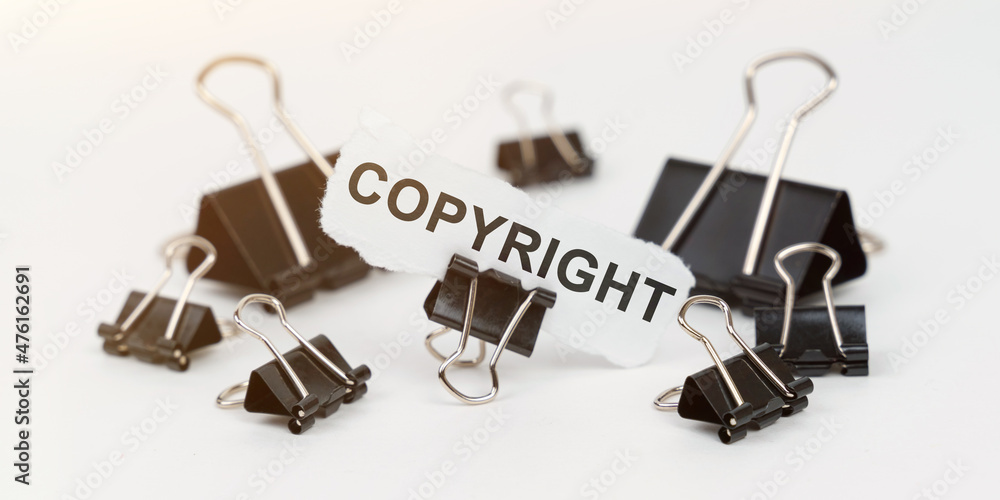 On a white table there are office clamps, in one clip there is paper with the inscription - COPYRIGHT On a white table there are office clamps, in one clip there is paper with the inscription - COPYRIGHT