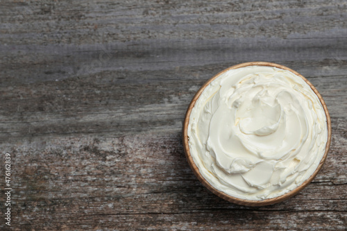 Bowl of tasty cream cheese on wooden table, top view. Space for text