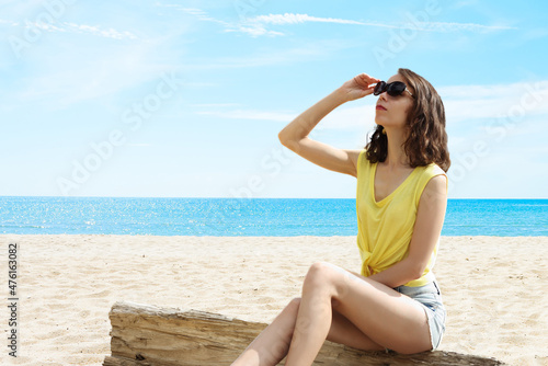 Girl on the beach in sunglasses looks into the sky. The concept of relaxation, vacation, pleasure.