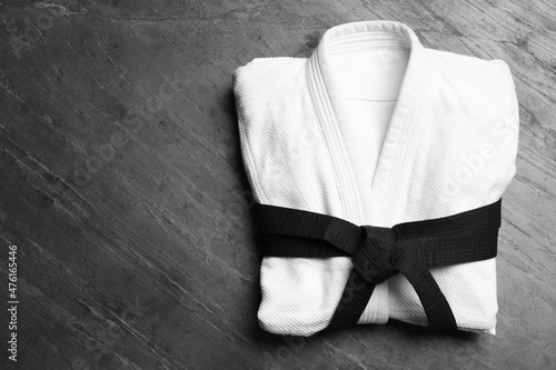 Martial arts uniform with black belt on grey stone background, top view. Space for text photo