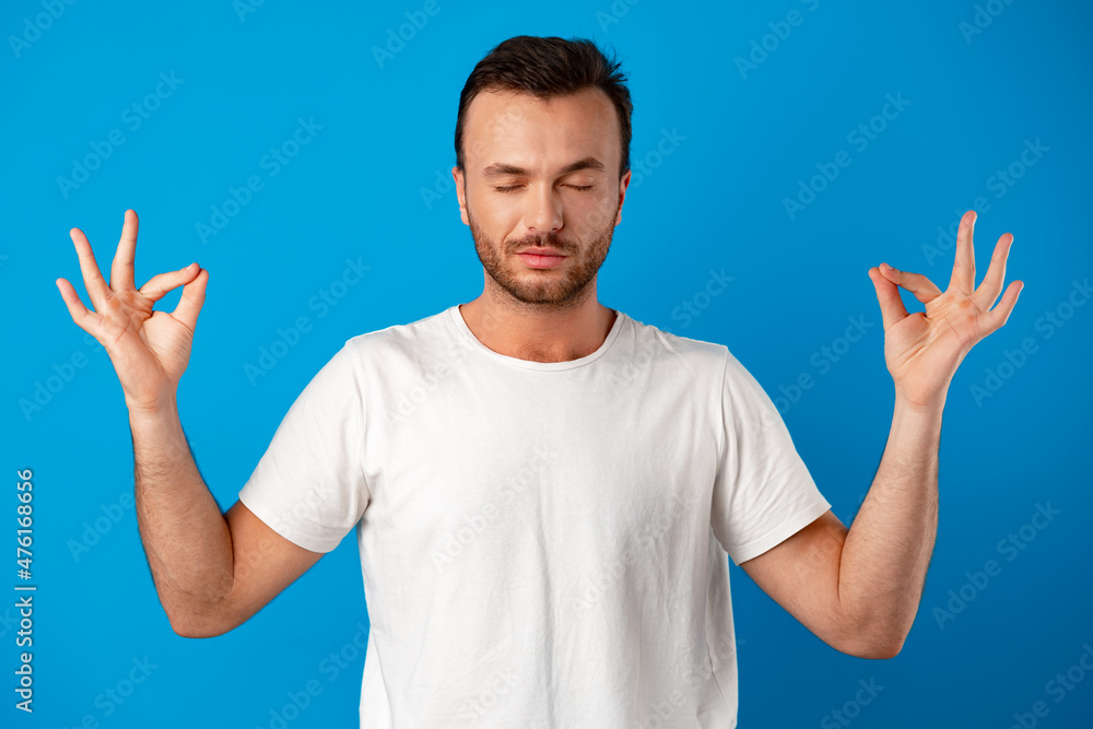 Focused handsome young man meditating on camera iover blue background Focused handsome young man meditating on camera iover blue background