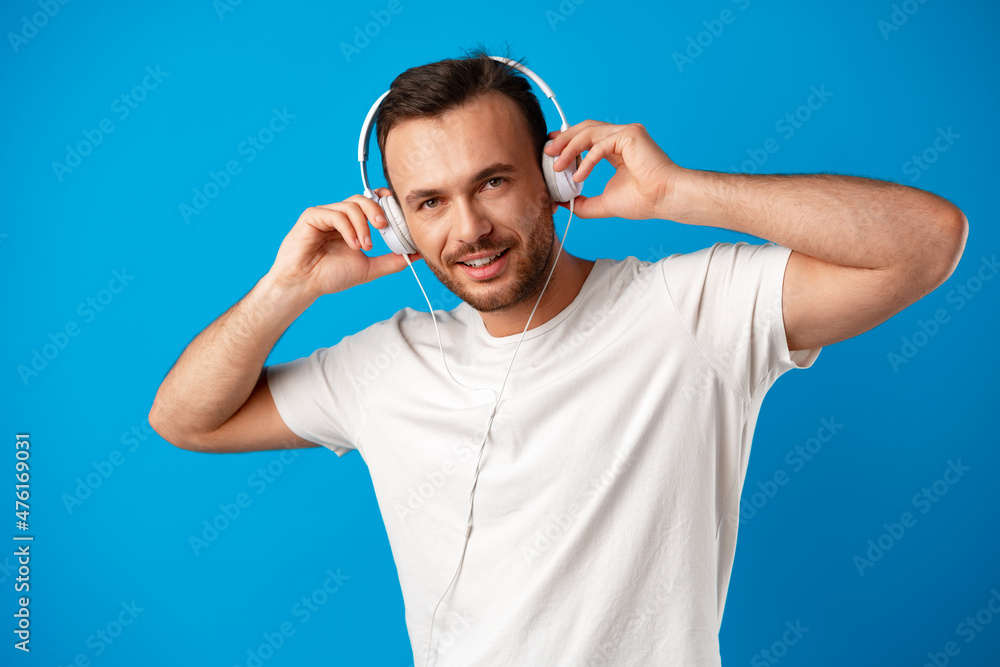 Fototapeta premium Young man listening to music with headphones on blue background.