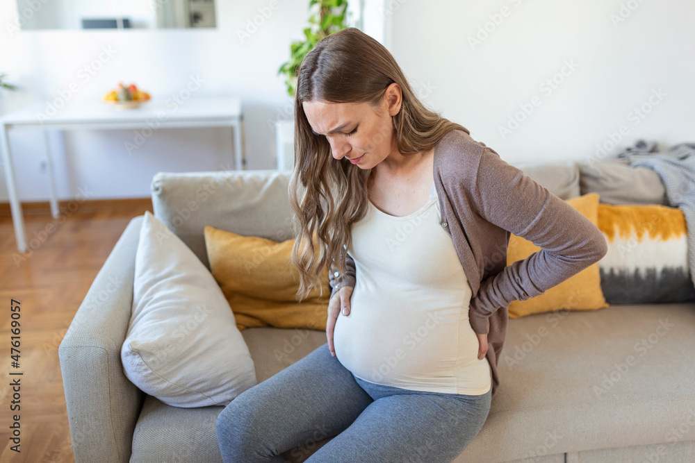 Young pregnant woman suffering from backpain or migraine, feeling sick, sitting on sofa at home, free space. Sad expecting lady touching her big tummy, home alone Young pregnant woman suffering from backpain or migraine, feeling sick, sitting on sofa at home, free space. Sad expecting lady touching her big tummy, home alone