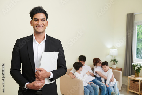 Portrait of happy real estate agent with documents standing in house he sold to family with two children