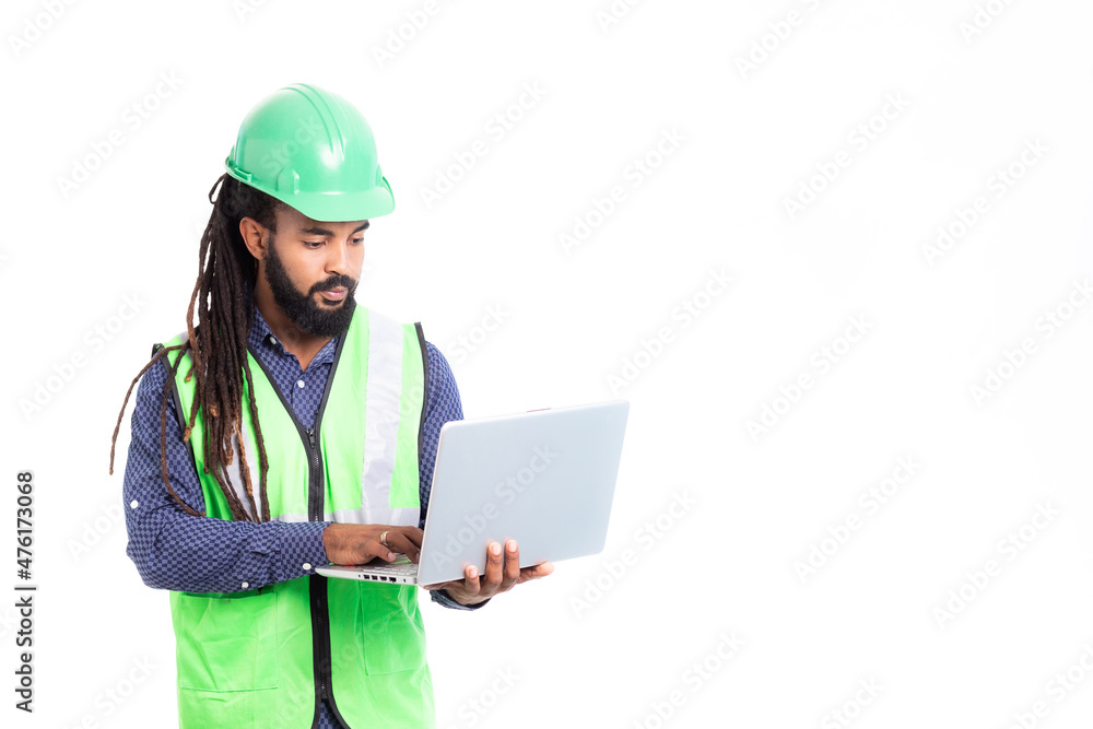 Caribbean man with dreadlocks and beard, married architect working with laptop, wearing blue shirt and phosphorescent green vest and green helmet Caribbean man with dreadlocks and beard, married architect working with laptop, wearing blue shirt and phosphorescent green vest and green helmet