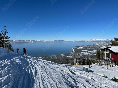 Scenic view of skiers and snowboarders on the snow covered slopes at a ski resort on a bluebird winter day, with Lake Tahoe in the distance