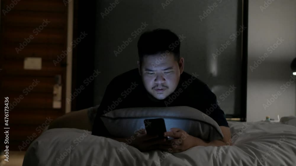 asian man while chatting on mobile phone and lay on the bed in bed room in night time asian man while chatting on mobile phone and lay on the bed in bed room in night time
