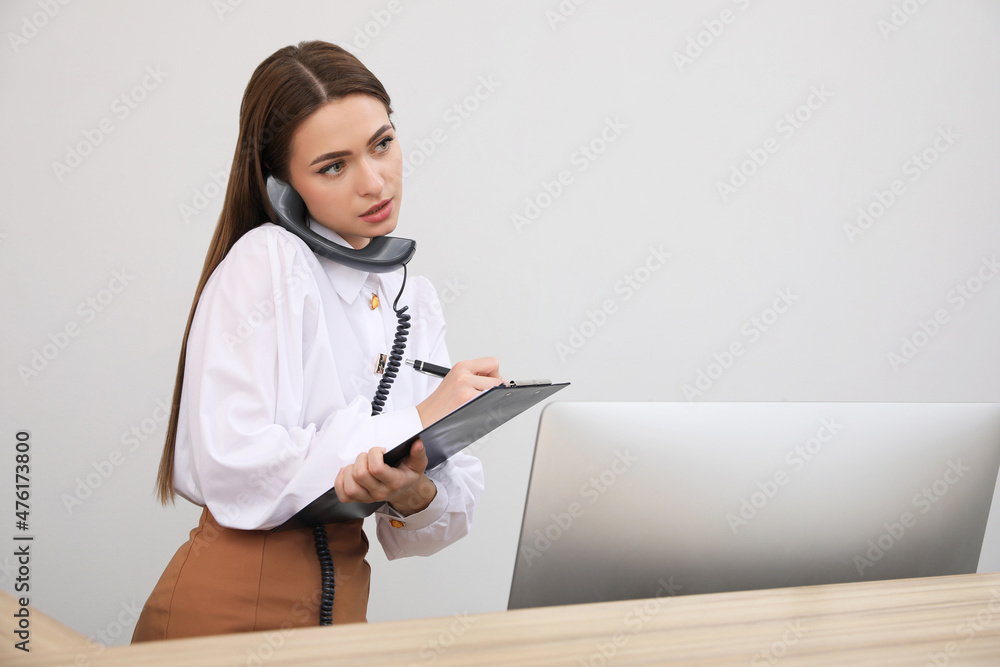 Female receptionist with clipboard talking on phone at workplace Female receptionist with clipboard talking on phone at workplace
