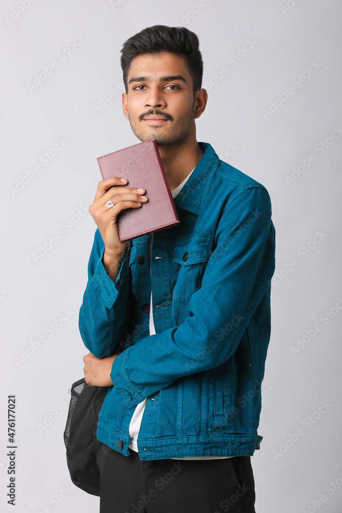 Young Indian man standing and holding dairy in hand on white background. Young Indian man standing and holding dairy in hand on white background.