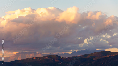 Beautiful fluffy clouds over the mountains on sunny day at golden hour painted with sun © Elena