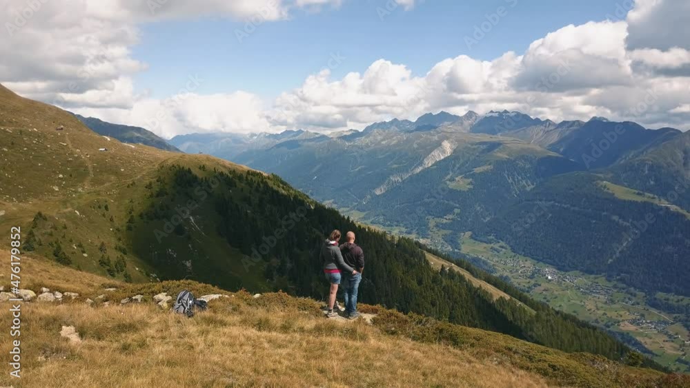 Drone shot rotating behind a couple man and woman standing on a mountain looking over a valley in Switzerland in 4k. Drone shot rotating behind a couple man and woman standing on a mountain looking over a valley in Switzerland in 4k.