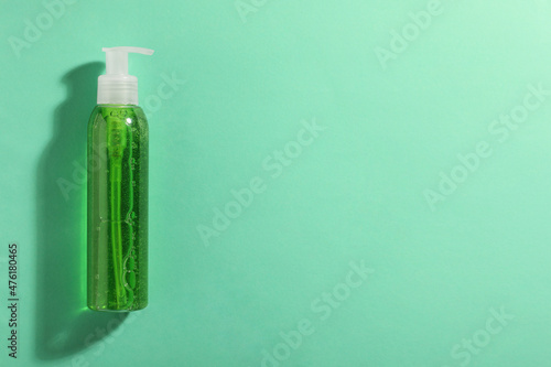 Bottle of green cosmetic gel on turquoise background, top view. Space for text