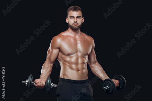 Sexy athletic man is showing muscular body with dumbbells standing with his head down  isolated over black background