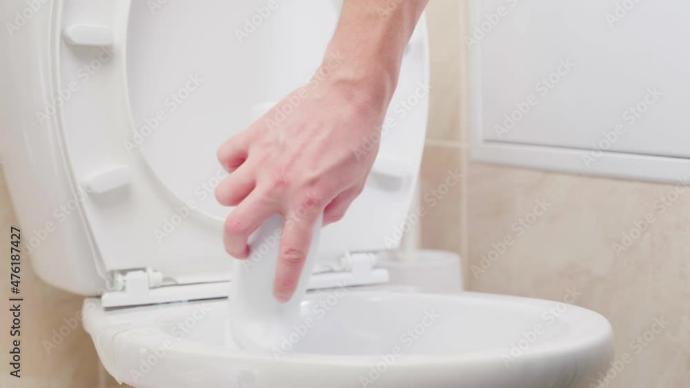 Disinfection of the toilet with a special compound. The hand lowers the container with the detergent into the toilet and goes along the perimeter of the rim Disinfection of the toilet with a special compound. The hand lowers the container with the detergent into the toilet and goes along the perimeter of the rim