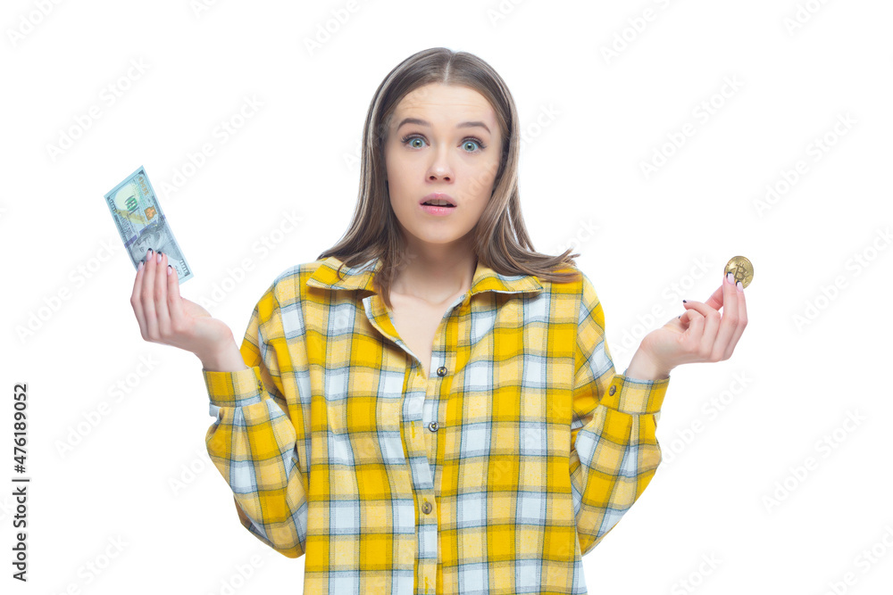 Shot of an astonished young female holding a golden bitcoin in one hand and dollar banknote in the other hand. Doubts where to invest, the choice of currency Shot of an astonished young female holding a golden bitcoin in one hand and dollar banknote in the other hand. Doubts where to invest, the choice of currency