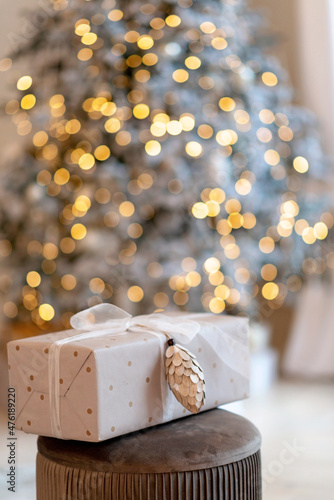 Gift box wrapped in wrapping paper with pine cone on background of new year lights bokeh christmas tree.Copy space. Soft selective focus. © Tasha Sinchuk