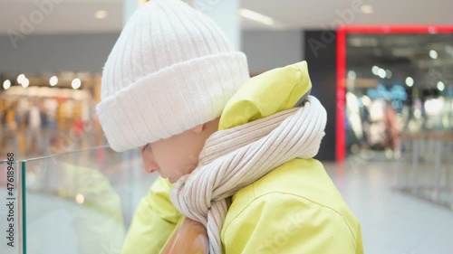 cute boy in yellow jacket, white hat and scarf in shopping mall looks mysteriously into distance in close-up. Christmas sale. Buying Christmas gifts. Weekend with family in the entertainment complex photo