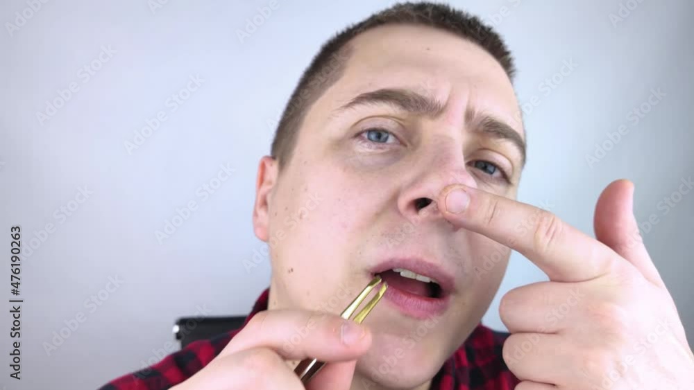Man pulls out his nose hair with tweezers. Close-up of male hygiene products. Isolated on white background. The male looks at the screen as if in a mirror. Man pulls out his nose hair with tweezers. Close-up of male hygiene products. Isolated on white background. The male looks at the screen as if in a mirror.