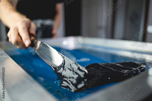 Ink spatula in hand of craftsman applying plastisol ink on screen printing machine 