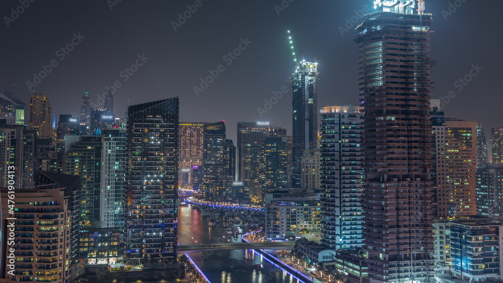 Dubai Marina with several boat and yachts parked in harbor and skyscrapers around canal aerial night timelapse.