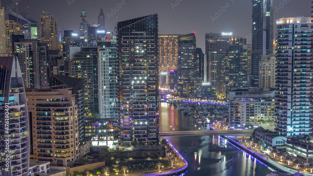 Fototapeta premium Dubai Marina with several boat and yachts parked in harbor and skyscrapers around canal aerial all night timelapse.