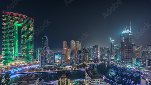 Dubai Marina with several boat and yachts parked in harbor and skyscrapers around canal aerial all night timelapse.