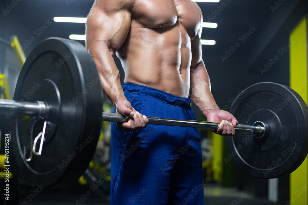 Close up of a naked muscular torso and strong man arms lifting a heavy barbell while training in a gym