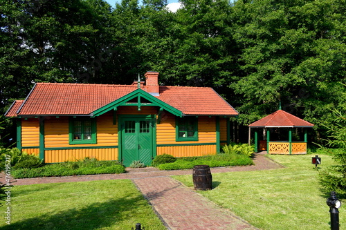 A close up on an old building made out of logs, planks and boards wih an angled roof made out of tiles located next to a small gazebo and a wooden barrel used for decorative purposes in Poland
