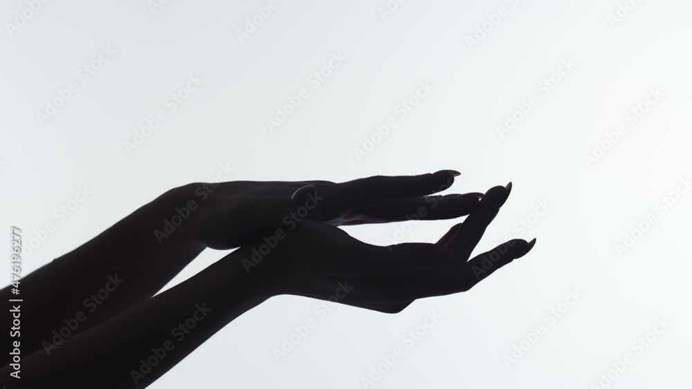 Closeup of the silhouette of woman's hands on white background, runs finger along arm after applying skin cosmetics. Cosmetics concept