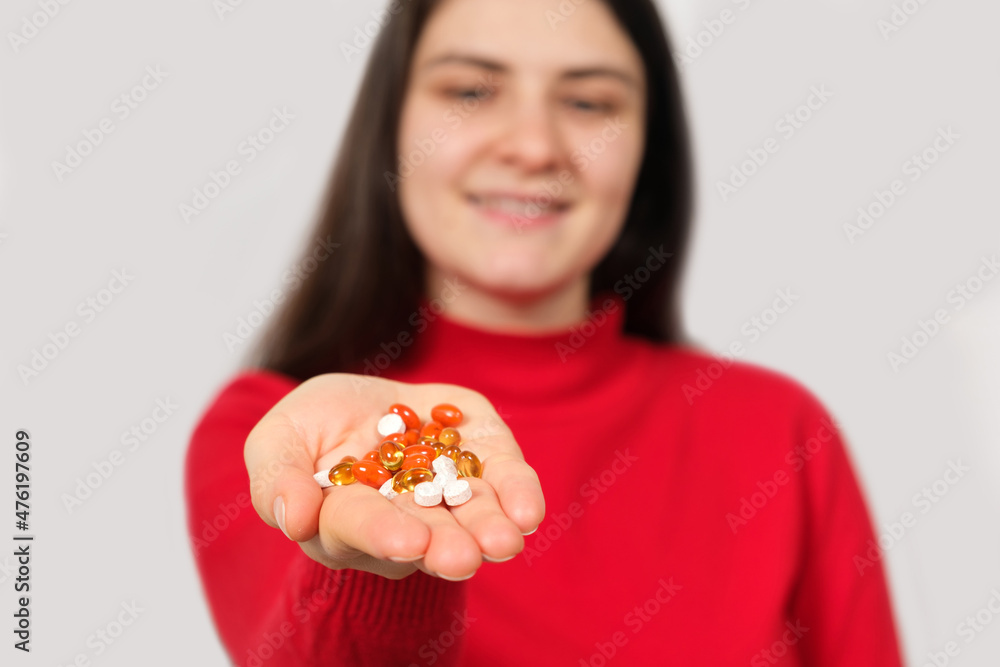A woman smiling stretches out her hand with a handful of colorful pills and capsules