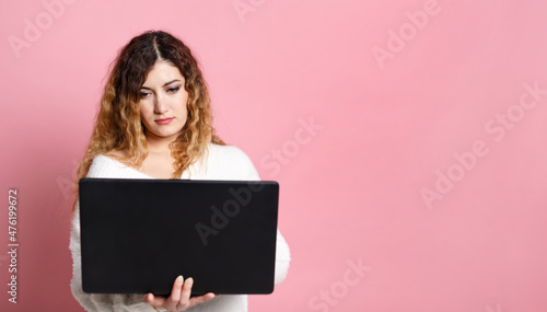 Woman standing isolated on a pink background using a laptop computer. With a place for a copy space.