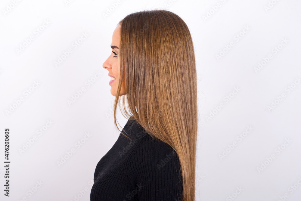 Obraz premium Profile of smiling Young caucasian girl wearing black turtleneck over white background with healthy skin, has contemplative expression, ready to have outdoor walk.